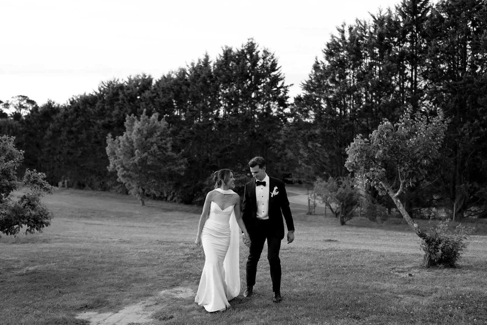 Black and white: a couple walking hand in hand along the edge of a field