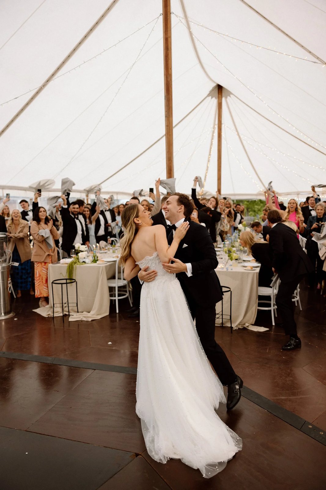 A couple dancing in a sailcloth marquee as guests cheer from their tables