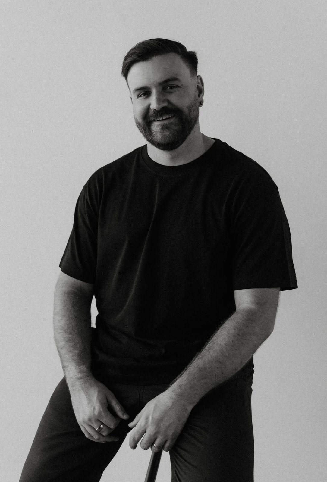 Black and white portrait of Matt Ashton in a black T-shirt, seated on a stool